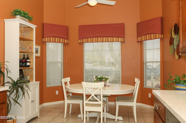 dining space featuring ceiling fan, light tile patterned flooring, a towering ceiling, and baseboards