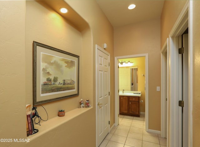 corridor featuring recessed lighting, a sink, baseboards, and light tile patterned floors