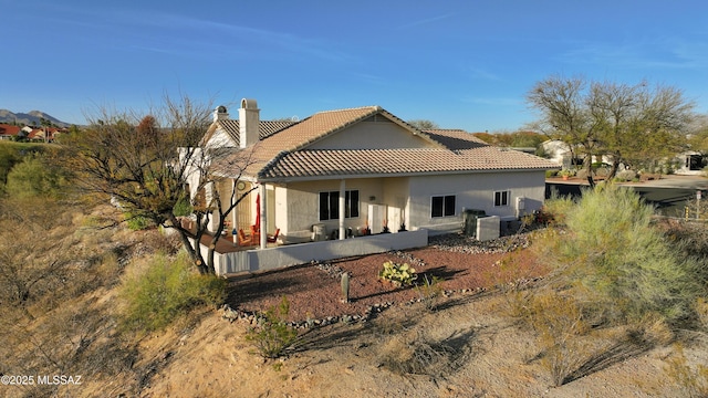 rear view of house with a patio, a chimney, a tiled roof, and stucco siding