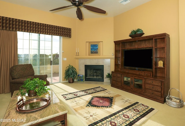 living area featuring a ceiling fan, visible vents, a tiled fireplace, and carpet flooring