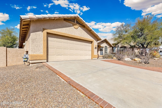 view of front facade with a garage, fence, driveway, a tiled roof, and stucco siding