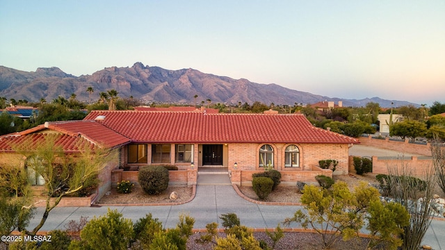 view of front of house with a tile roof, a mountain view, a chimney, and brick siding