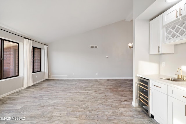 interior space with beverage cooler, a sink, visible vents, white cabinets, and vaulted ceiling