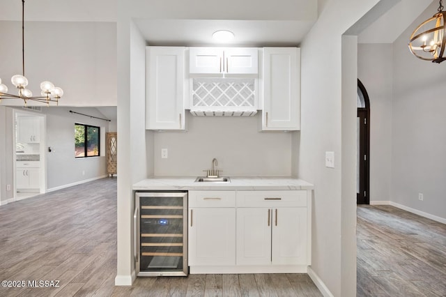 bar featuring wine cooler, indoor wet bar, light wood-style flooring, an inviting chandelier, and a sink