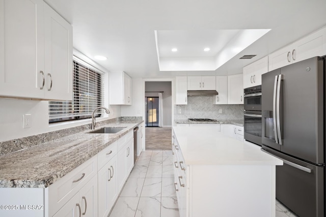 kitchen featuring under cabinet range hood, a sink, marble finish floor, appliances with stainless steel finishes, and a tray ceiling