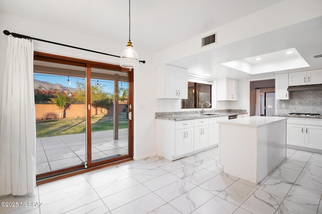 kitchen with a sink, marble finish floor, light countertops, under cabinet range hood, and backsplash