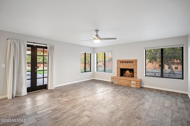 unfurnished living room featuring french doors, a brick fireplace, wood finished floors, and a healthy amount of sunlight