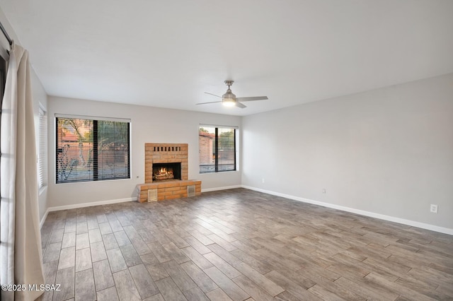 unfurnished living room with a ceiling fan, a fireplace, baseboards, and wood finished floors