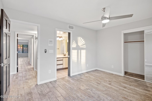 unfurnished bedroom featuring baseboards, visible vents, ensuite bath, light wood-style floors, and a closet