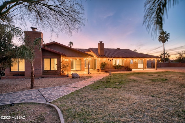 back of property at dusk with fence, a yard, a chimney, and a patio