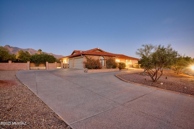 mediterranean / spanish house with a tile roof, concrete driveway, a gate, fence, and a garage