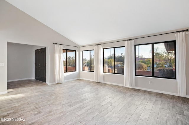 unfurnished room featuring light wood-style floors, baseboards, and vaulted ceiling