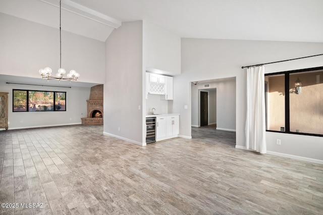 unfurnished living room with a notable chandelier, beverage cooler, baseboards, a brick fireplace, and light wood finished floors