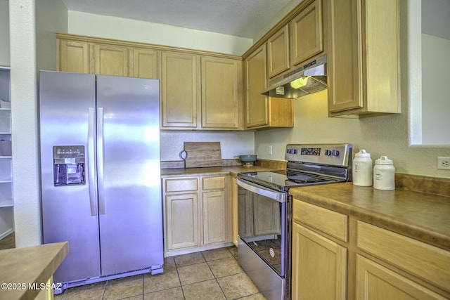 kitchen featuring dark countertops, under cabinet range hood, light tile patterned floors, and appliances with stainless steel finishes