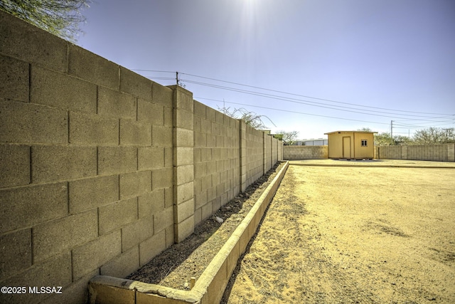 view of yard featuring an outbuilding, a fenced backyard, driveway, and a storage shed