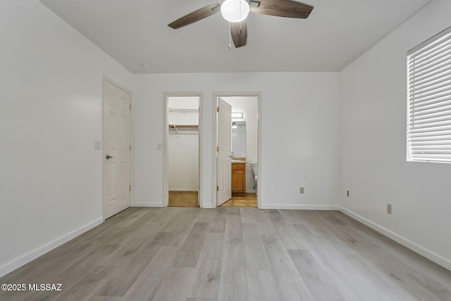 unfurnished bedroom with baseboards, light wood-style flooring, ceiling fan, a spacious closet, and a closet