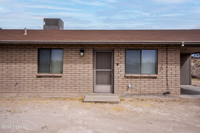 exterior space featuring a shingled roof, cooling unit, and brick siding