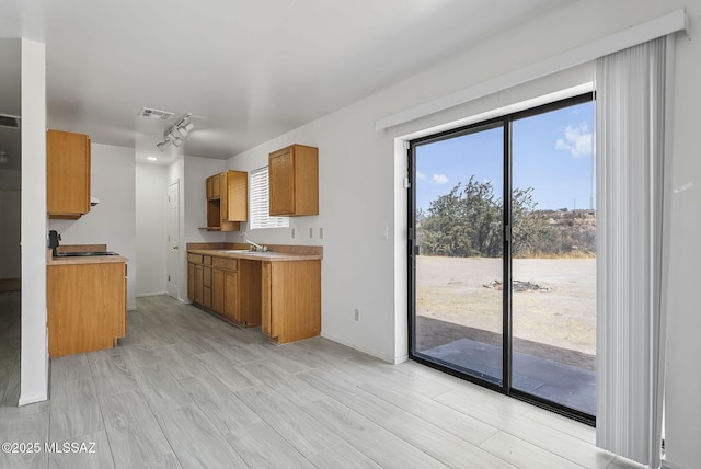 kitchen featuring visible vents, brown cabinetry, a sink, and light countertops