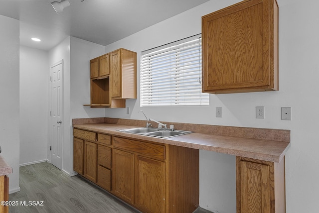 kitchen featuring baseboards, wood finished floors, a sink, and brown cabinets