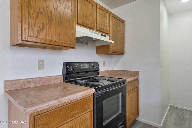 kitchen with electric range, baseboards, brown cabinets, light countertops, and under cabinet range hood