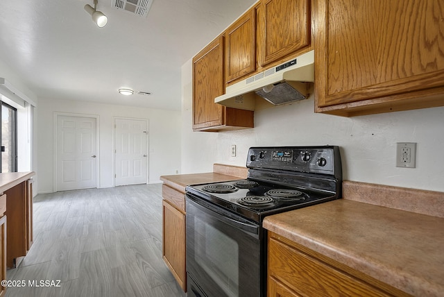 kitchen with light wood finished floors, visible vents, brown cabinetry, under cabinet range hood, and black / electric stove