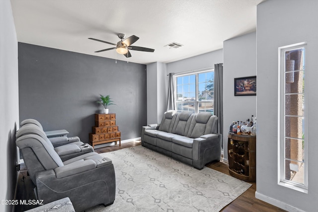 living room with a ceiling fan, visible vents, wood finished floors, and baseboards
