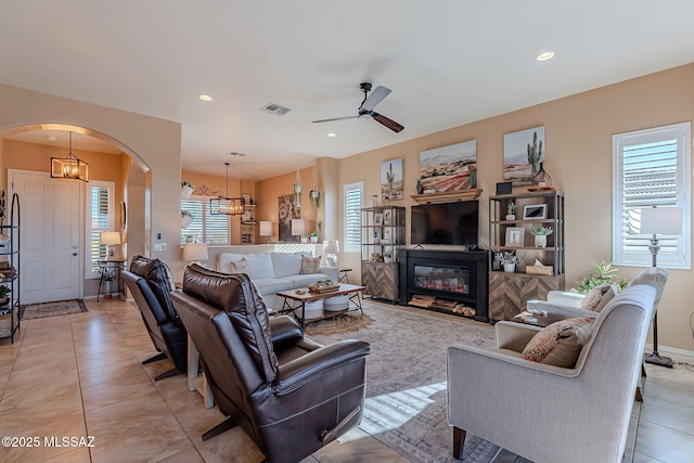 living room featuring visible vents, a glass covered fireplace, recessed lighting, arched walkways, and light tile patterned floors