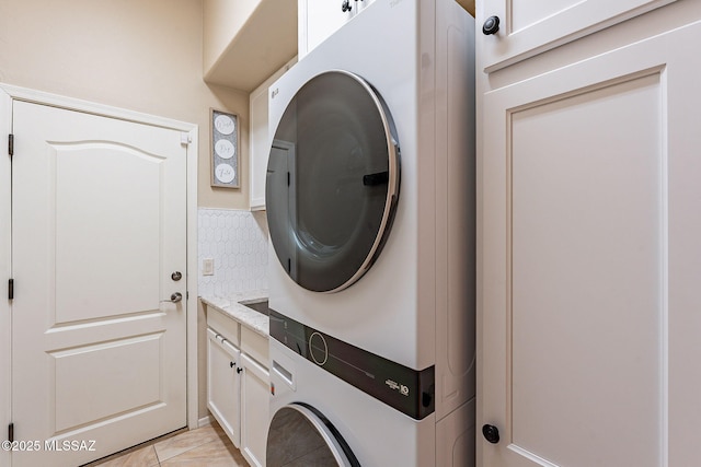 laundry area featuring light tile patterned floors, stacked washer / dryer, and cabinet space