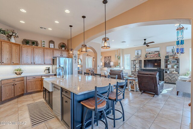 kitchen featuring visible vents, an island with sink, arched walkways, a sink, and appliances with stainless steel finishes