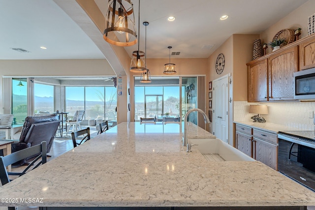 kitchen with stainless steel microwave, range with electric cooktop, visible vents, a large island, and a sink