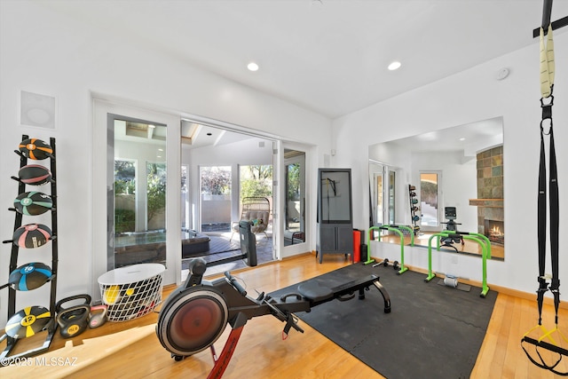 workout room with baseboards, a stone fireplace, wood finished floors, and recessed lighting