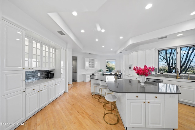 kitchen featuring a raised ceiling, white cabinetry, light wood finished floors, and decorative backsplash