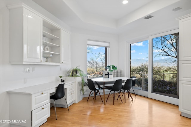 dining space featuring visible vents, built in study area, a tray ceiling, light wood-style floors, and recessed lighting