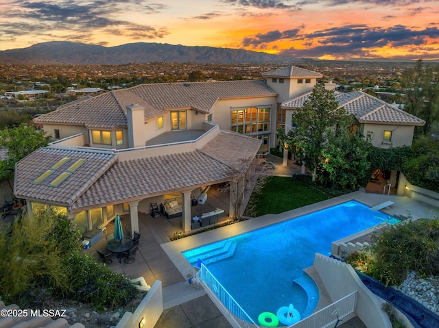 back of property at dusk with a balcony, a tile roof, a mountain view, and stucco siding