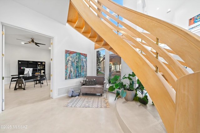 sitting room with ceiling fan, concrete floors, a high ceiling, and stairs