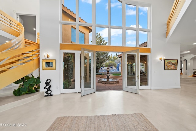 foyer featuring concrete flooring, arched walkways, french doors, and a high ceiling