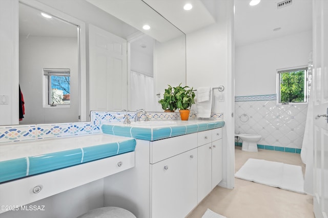 bathroom featuring toilet, recessed lighting, a wainscoted wall, vanity, and tile walls