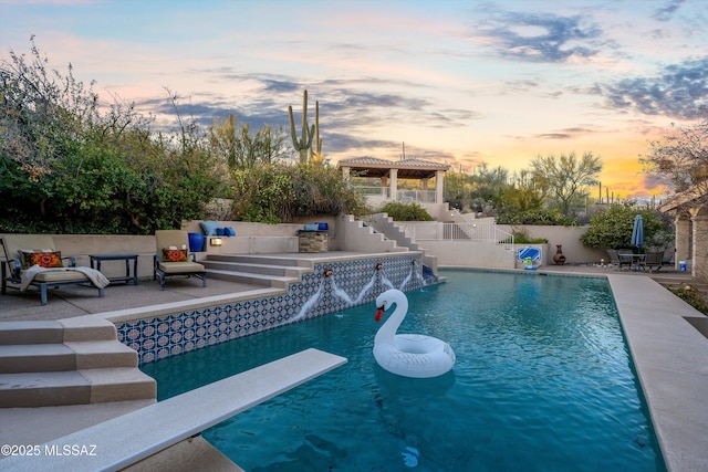 pool at dusk featuring a diving board, outdoor lounge area, a patio area, and a fenced in pool