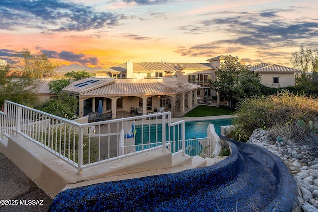 back of house with a tile roof, a patio area, an outdoor pool, and stucco siding