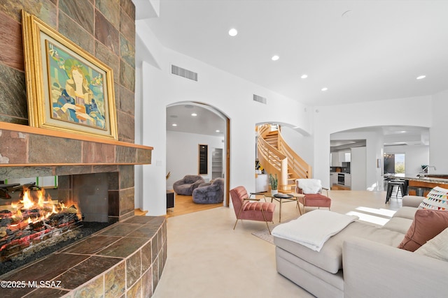 living area with arched walkways, a tile fireplace, visible vents, and recessed lighting