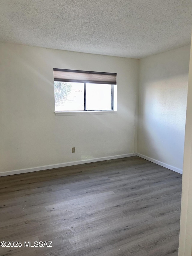 spare room featuring a textured ceiling, baseboards, and wood finished floors