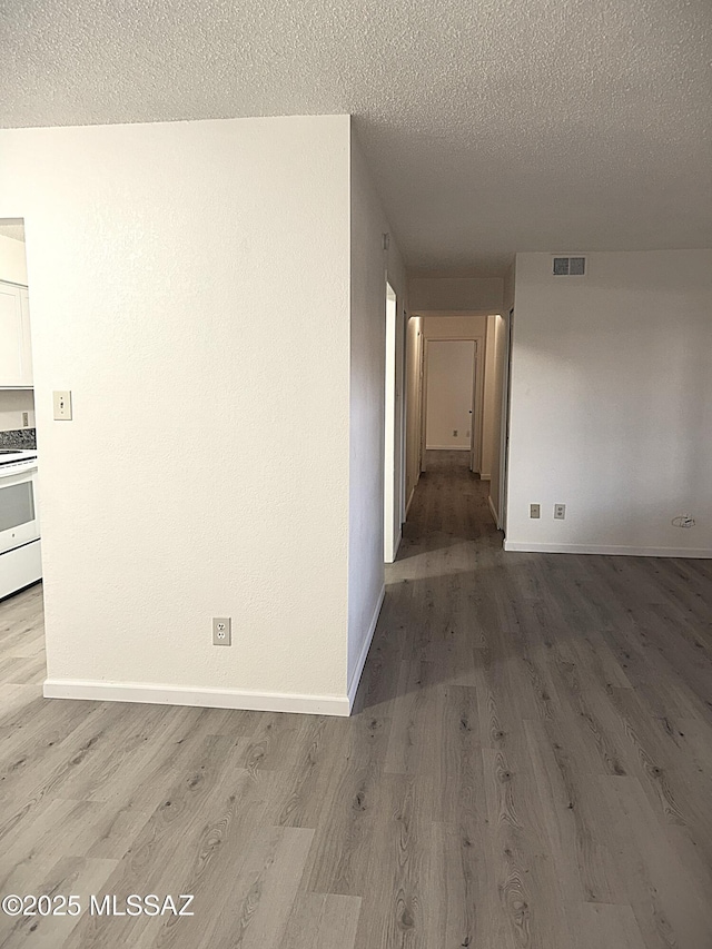 hall featuring visible vents, a textured ceiling, baseboards, and wood finished floors