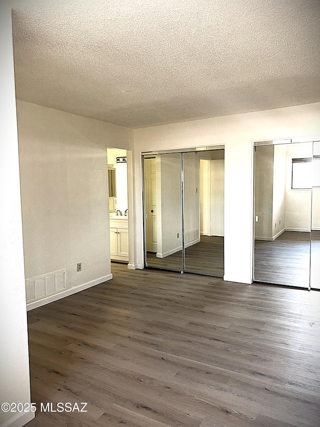 unfurnished bedroom with multiple closets, visible vents, a textured ceiling, and dark wood-type flooring