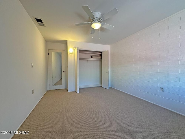 unfurnished bedroom featuring a closet, visible vents, brick wall, baseboards, and light colored carpet