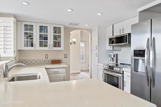 kitchen with a sink, arched walkways, appliances with stainless steel finishes, and light countertops