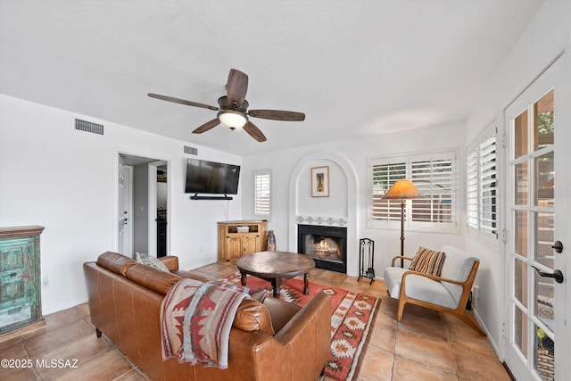 living room featuring a tiled fireplace, visible vents, and a ceiling fan