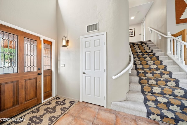 entryway featuring stairs, baseboards, visible vents, and a towering ceiling