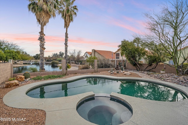 pool at dusk featuring a pool with connected hot tub and a fenced backyard