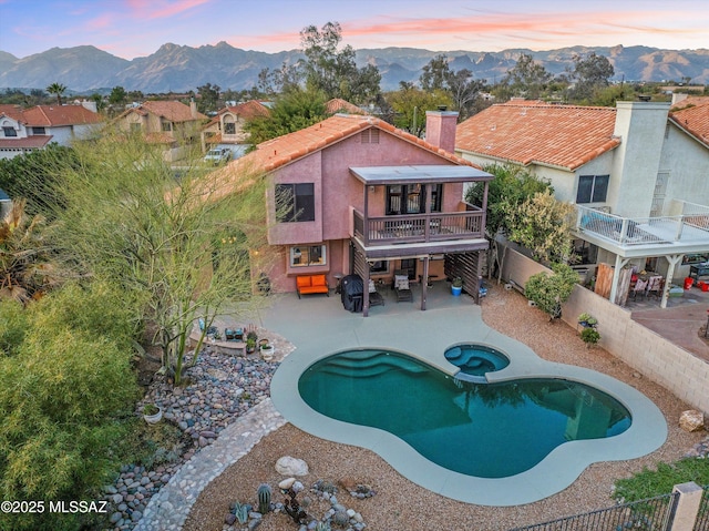 pool at dusk with a fenced backyard, a mountain view, a pool with connected hot tub, and a patio