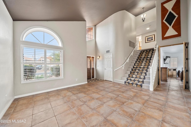 entryway with visible vents, stairway, light tile patterned flooring, baseboards, and a towering ceiling